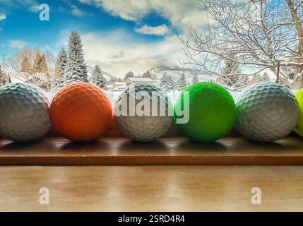 Golfbälle auf der Fensterbank bieten einen gerahmten Blick auf die Schneelandschaft mit Kiefern, Bergen, blauem Himmel und Wolken. Der Golfplatz liegt im Vordergrund und im Schnee. Stockfoto