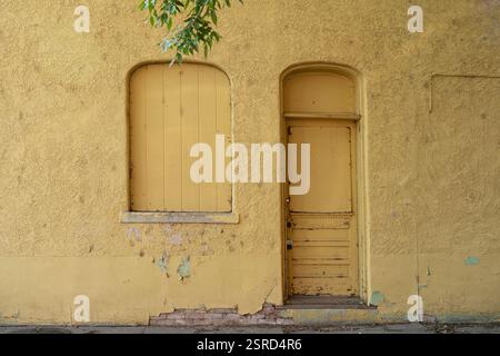Die alte Putzfassade des alten Architekturgebäudes ist senfgelb gestrichen. Die an Bord befindliche Fenstertür hat ein gewölbtes Design. Siehe Blätter. Stockfoto