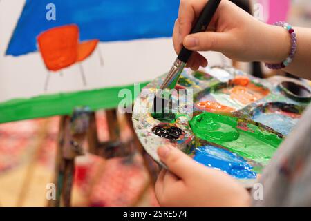 Das Kind mischt grüne Farbe auf der Palette. Kunstkurs im Gange. Stockfoto