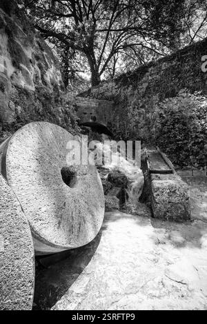 Eine alte Steinwassermühle im Krka-Nationalpark, Kroatien, mit Mühlsteinen, die neben einem rauschenden Bach ruhen, in Schwarz-weiß gefangen. Stockfoto