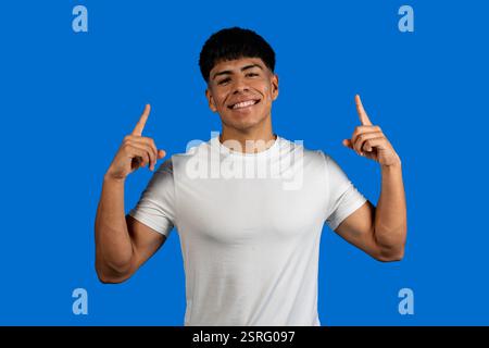 Ein lächelnder junger Mann, der mit beiden Zeigefingern auf blauem Hintergrund zeigt Stockfoto