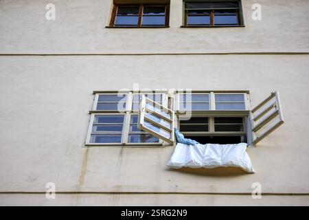 Ein Fragment eines zweistöckigen Gebäudes mit vier Fenstern, von denen eines mit offenen Jalousien und einem hängenden weißen Tuch dekoriert ist. Stockfoto
