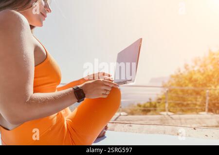Junge Frau in Orange Sportswear benutzt Laptop im Freien Stockfoto