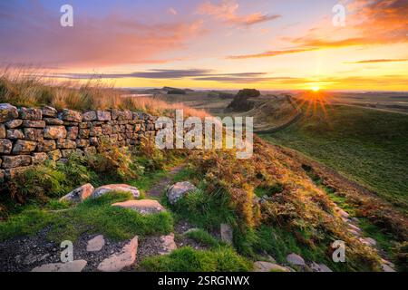 Lebhafter Sommersonnenaufgang an der Hadrians Wall mit Blick auf Cuddy's Crags, während die Sonne über den Horizont kommt. Northumberland, Großbritannien. Stockfoto