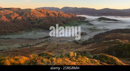 Goldenes Licht bei Sonnenaufgang, das Berggipfel um Little Langdale Tarn trifft, während sich der Herbstnebel in den Tälern füllt. Lake District, Großbritannien. Stockfoto