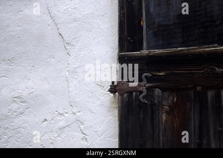 Antikes, geschmiedetes Türscharnier aus Metall, das eine verwitterte Holztür hält, die mit dem Alter verdunkelt wurde. Kopierbereich für Text. Stockfoto