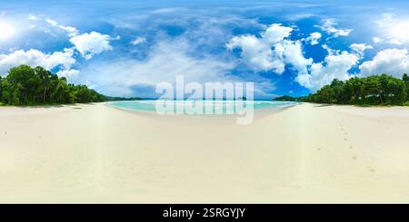 Ein riesiger Strand erstreckt sich unter einem hellen Himmel mit türkisfarbenem Wasser, das auf weichem Sand trifft, eingerahmt von üppigem Grün auf beiden Seiten. Grand Anse Beach, Seychellen. VR 360. Stockfoto