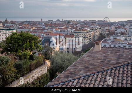 Über den Terrakotta-Dächern von Nizza, Frankreich, erstreckt sich das Mittelmeer bis zum Horizont, das bei Sonnenuntergang in sanftem Winterlicht getaucht ist. Stockfoto