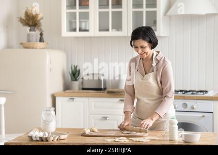 Glückliche ältere Bäckerin, die Teig in der modernen Küche flacht Stockfoto