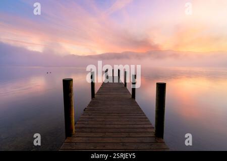 Holzsteg auf einem ruhigen nebeligen See bei Sonnenaufgang, Derwentwater, Lake District, Großbritannien. Stockfoto