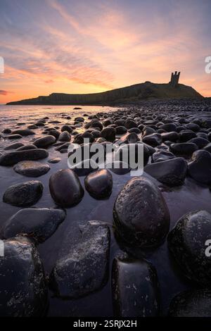 Farbenfroher Sonnenaufgang am Dunstanburgh Castle mit Felsen an der Küste von Northumbria, Großbritannien. Stockfoto