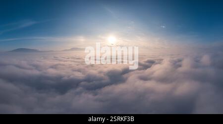 Der Panoramablick auf den Sonnenaufgang, der über dem flauschigen, bewölkten Himmel strahlt, schafft eine ruhige und ruhige Atmosphäre Stockfoto