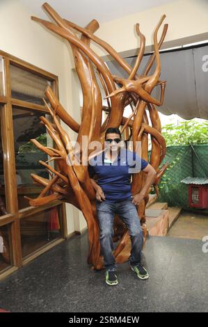 Mann sitzt auf Holzbaumskulptur, trivandrum, kerala, Indien, Asien, MR#801B, Asien Stockfoto