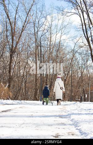 Unbekannte Mutter und Sohn mit Schlittenlaufen im Winterpark. Junge zieht Schlitten mit Mutter im schneebedeckten Park. Winteraktivität. Familienleben. Kleinkind mit Mutter Stockfoto