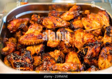 Glasierte Hähnchenflügel in einem Edelstahltablett mit goldbrauner, knuspriger Textur Stockfoto