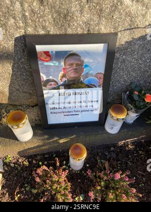 Flensburg, Schleswig-Holstein das Bild zeigt einen Gedenkstein im Carlisle-Park in Flensburg mit der Inschrift den Opfern der Gewaltherrschaft. Vor dem Stein liegen eine Kranzniederlegung mit Tannenzweigen und Zapfen sowie eine blau-gelbe Schleife, die auf die Ukraine hindeuten könnte. Daneben stehen mehrere Grablichter und ein gerahmtes Foto mit einer Gedenkinschrift zu Alexej Nawalny. Die Szenerie ist von Sonnenlicht durchziehen, wobei Baumäste Schatten auf den Stein werfen. Änd. 16. Februar jährt sich der Todestag des russischen Oppositionsführers Alexej Nawalny. Er starb am 16. Februar 2024 i Stockfoto