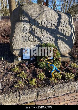 Flensburg, Schleswig-Holstein das Bild zeigt einen Gedenkstein im Carlisle-Park in Flensburg mit der Inschrift den Opfern der Gewaltherrschaft. Vor dem Stein liegen eine Kranzniederlegung mit Tannenzweigen und Zapfen sowie eine blau-gelbe Schleife, die auf die Ukraine hindeuten könnte. Daneben stehen mehrere Grablichter und ein gerahmtes Foto mit einer Gedenkinschrift zu Alexej Nawalny. Die Szenerie ist von Sonnenlicht durchziehen, wobei Baumäste Schatten auf den Stein werfen. Änd. 16. Februar jährt sich der Todestag des russischen Oppositionsführers Alexej Nawalny. Er starb am 16. Februar 2024 i Stockfoto