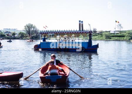 Butlin Queen of the Lake Vergnügungsboot auf dem See von Butlin's Minehead Ferienort im Jahr 1978, mit zwei Jungen in einem Ruderboot und verschiedenen Kanus Stockfoto