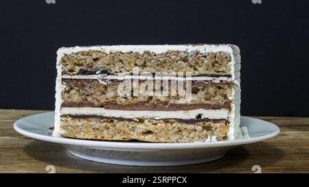 Ein wunderschön gefertigter, mehrschichtiger Kuchen mit Sahne und Nüssen sitzt auf einem Teller und unterstreicht seine ansprechenden Texturen und Aromen. Stockfoto