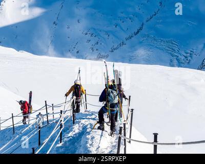 Chamonix-Mont-Blanc, Frankreich, 21. Januar 2025. Gleitschirmflieger mit Rucksäcken und einem Fallschirm im Inneren steigen den steilen, schneebedeckten Hang der A hinab Stockfoto