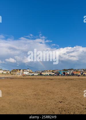 Perranporth, Cornwall, England, Großbritannien - 5. Juni 2022: Häuser in der Nähe von Perranporth Beach mit einem Regenbogen im Hintergrund Stockfoto