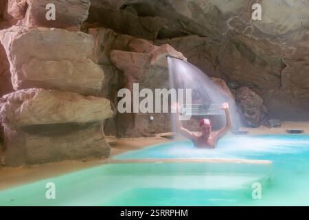 Ein Mann mit einer weißen und roten Kappe unter einem Wasserfall in einem Spa in einer Höhle in der Toskana, Italien Stockfoto