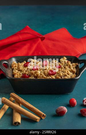 Ein goldener Apfel- und Preiselbeerknusprig, serviert in einem schwarzen gusseisernen Gericht, garniert mit leuchtenden roten Fruchtstücken und knusprigen Haferbröseln Stockfoto