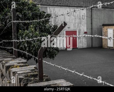 Stacheldrahtzaun vor einem Lagerhaus mit roter Tür. Diese Grenze dient als Abschreckung für Einbrecher zum Schutz von Unternehmensgütern. Stockfoto