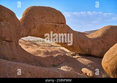 Natürlicher Granit-Felsenbogen, der einen Blick auf die weiten trockenen Wüstenebenen unter einem strahlend blauen Himmel in Spitzkoppe, Erongo-Region, Namibia, einrahmt Stockfoto