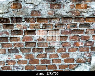 Strukturierte Ziegelwand mit unterschiedlichen Farbtönen und verwitterten Oberflächen in einer urbanen Umgebung während der Tageslichtstunden Stockfoto