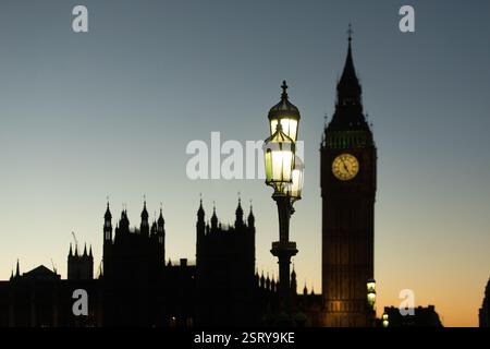 Beleuchtete Straßenlaternen stehen in der Dämmerung vor den Houses of Parliament und Big Ben in London. Stockfoto