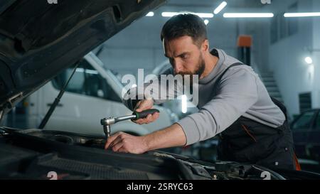 Professioneller Automechaniker Kaukasischer Mann, der in der Fahrzeugwartung arbeitet Motorspezialist, der Motorauto mit einem Schraubenschlüssel fixiert Stockfoto