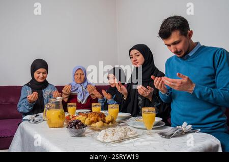 Muslimische Familie macht iftar dua zum Fastenbrechen während des Ramadan glückliche Eltern beim Abendessen mit ihren Kindern und Großmutter zu Hause am Esstisch Stockfoto