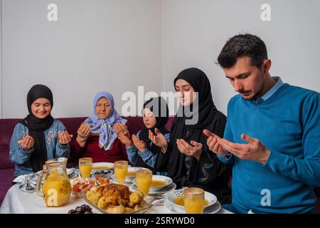 Muslimische Familie macht iftar dua zum Fastenbrechen während des Ramadan glückliche Eltern beim Abendessen mit ihren Kindern und Großmutter zu Hause am Esstisch Stockfoto