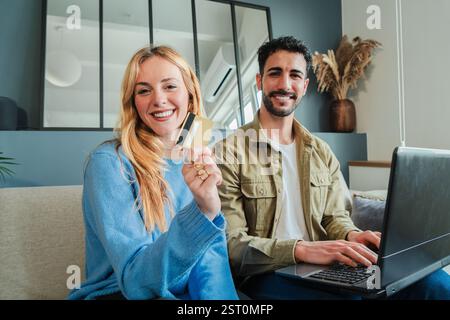 Glückliche Paare, die ihre Kreditkarte beim Online-Shopping zusammen mit Einem Laptop in gemütlicher Atmosphäre nutzen, ihre Zeit genießen und bequem und fröhlich miteinander einkaufen. Hochwertige Fotos Stockfoto