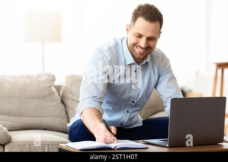 Mann, der zu Hause einen Laptop benutzt und Notizen schreibt Stockfoto