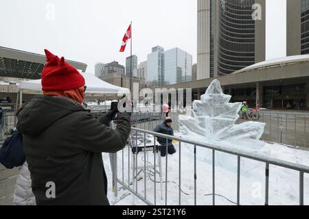 Toronto, Kanada, 15. Februar 2025. Ein Eisbildhauer schuf am 15. Februar 2025 eine Ahornblatt-Eisskulptur unter einer riesigen kanadischen Flagge auf dem Platz der Toronto City Hall in Toronto, Kanada. Am 15. Februar wurde vor dem Rathaus eine riesige kanadische Flagge mit einer Länge von 30 Metern und einer Breite von 15 Metern gehisst, um den 60. Jahrestag der Einweihung der kanadischen Flagge zu feiern. Quelle: Yu Ruidong/China News Service/Alamy Live News Stockfoto
