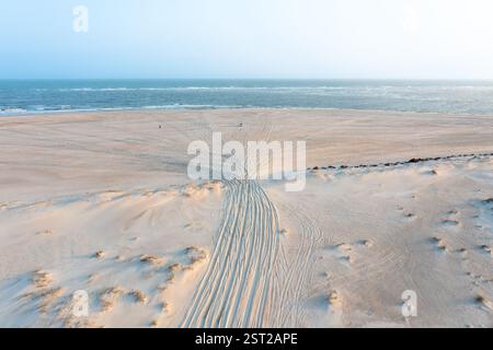 Aus der Vogelperspektive auf Reifenspuren im Sand, die zum Strand und zum Meer führen Stockfoto