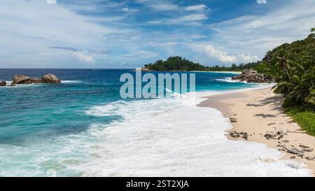 Wellen krachen auf Sandstrand mit Palmen und smaragdgrünem Wasser, das den Himmel reflektiert. Anse Boileau. Seychellen, Mahe. Stockfoto