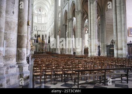 Weitläufige Innenausstattung der Kathedrale mit Holzstühlen, gotischen Bögen und atemberaubenden Buntglasfenstern im Hintergrund. Stockfoto