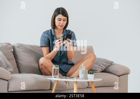 Auf dem Sofa sitzen und sich schminken. Die junge Frau ist zu Hause. Vorstellung von Schönheit. Stockfoto