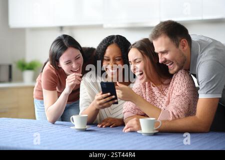 Lustige interrassische Gruppe von Freunden, die zu Hause in der Küche telefonieren Stockfoto