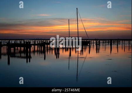 Das Segelboot legte während des Sonnenuntergangs an einem Yachthafen an, mit ruhigen Wasserreflexionen Stockfoto