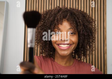 Eine junge Frau, die einen Make-up-Pinsel hält und lächelt Stockfoto