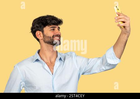 Lächelnder Geschäftsmann, der ein Selfie mit Smartphone auf gelbem Hintergrund macht Stockfoto