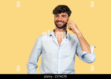 Porträt eines jungen Geschäftsmannes, der lächelt, während er auf dem Smartphone spricht, auf gelbem Hintergrund Stockfoto
