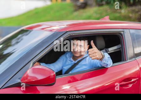 Lächelnder Fahrer in seinem Auto, der die Daumen hoch hält. Männlicher Fahrer, der während der Fahrt die Daumen nach oben zeigt Stockfoto