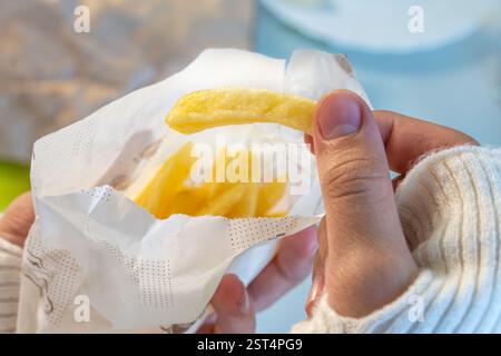 Anonyme Frau isst gerne Pommes im Restaurant. Hand hält Pommes Frites in Nahaufnahme. Essen von Junk Food in einem Fast-Food-Café. Stockfoto
