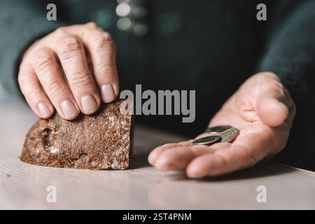 Ein älterer Mann hält Münzen und ein Stück trockenes Brot in der Hand. Das Konzept von Armut und Ernährungsknappheit für Rentner. Stockfoto
