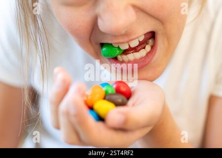 Sucht nach Süßigkeiten und Süßigkeiten. Bunte Süßigkeiten in den Händen und in den Zähnen des Mädchens. Der Schaden von Süßigkeiten für die Zähne. Stockfoto